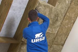 Homme posant de l'isolant en laine de verre de la marque URSA TERRA dans un grenier.
