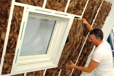 Personne installant de l'isolant en laine de verre dans ses combles.